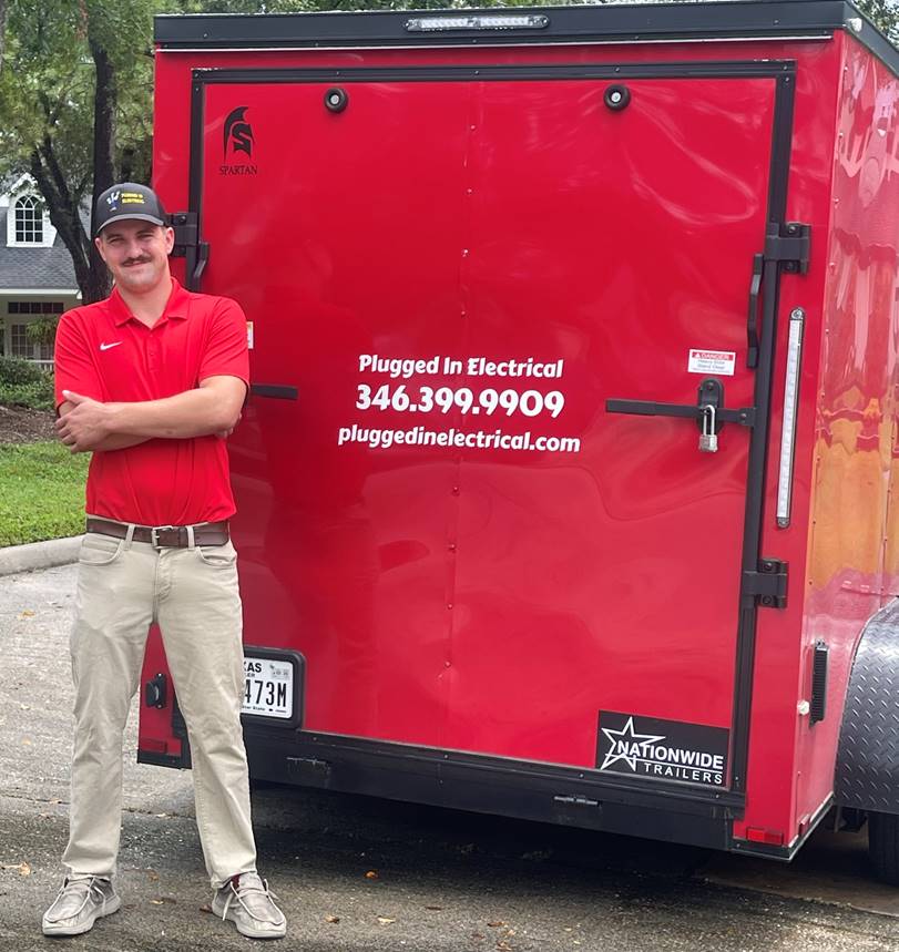 Pluggedin Electrical- A man stands beside a red enclosed trailer